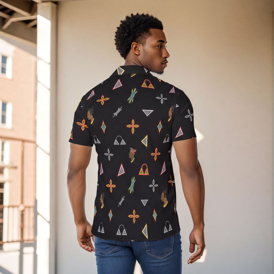 A man wearing a black shirt with a colorful geometric pattern stands in front of a white wall.