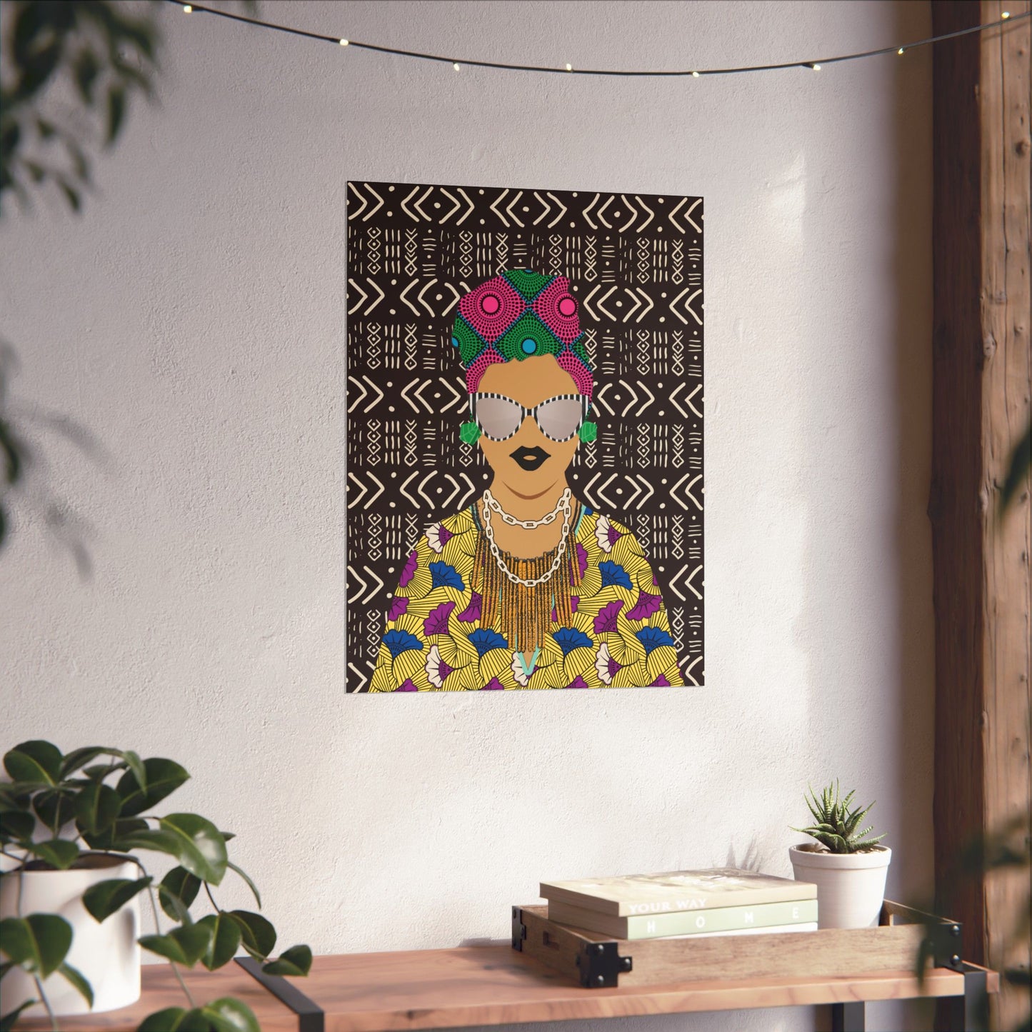 a colorful poster of a woman with a headdress, hanging on a wall above a wooden table with plants and books.