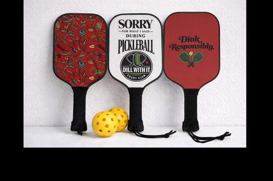 Three colorful paddleboards with different designs and text are displayed against a white wall, accompanied by two yellow balls.