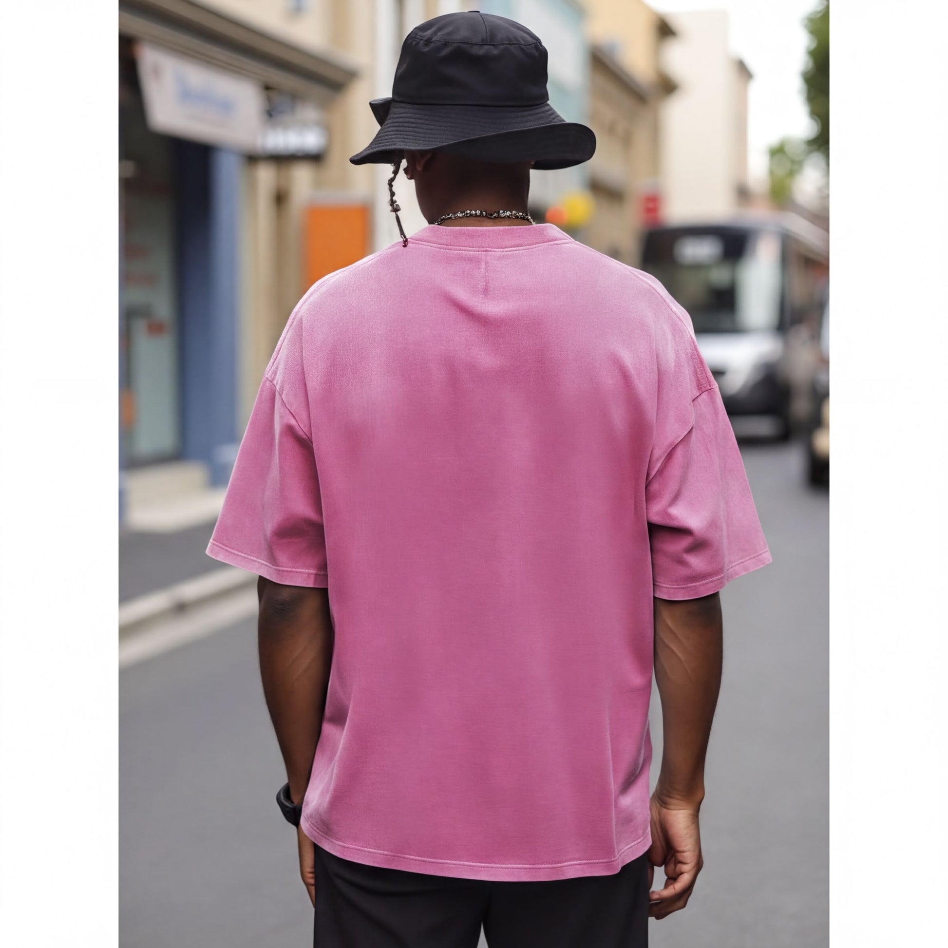 A person wearing a pink t-shirt and a black bucket hat is standing on a street, facing away from the camera.