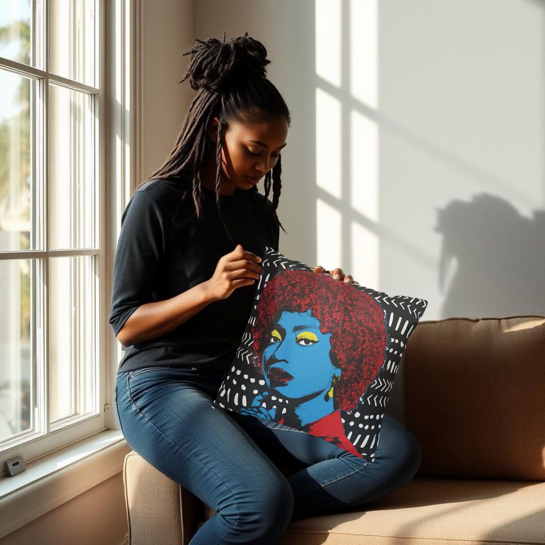 A woman with dreadlocks is sitting on a couch, holding a colorful pillow with a portrait of a woman on it.