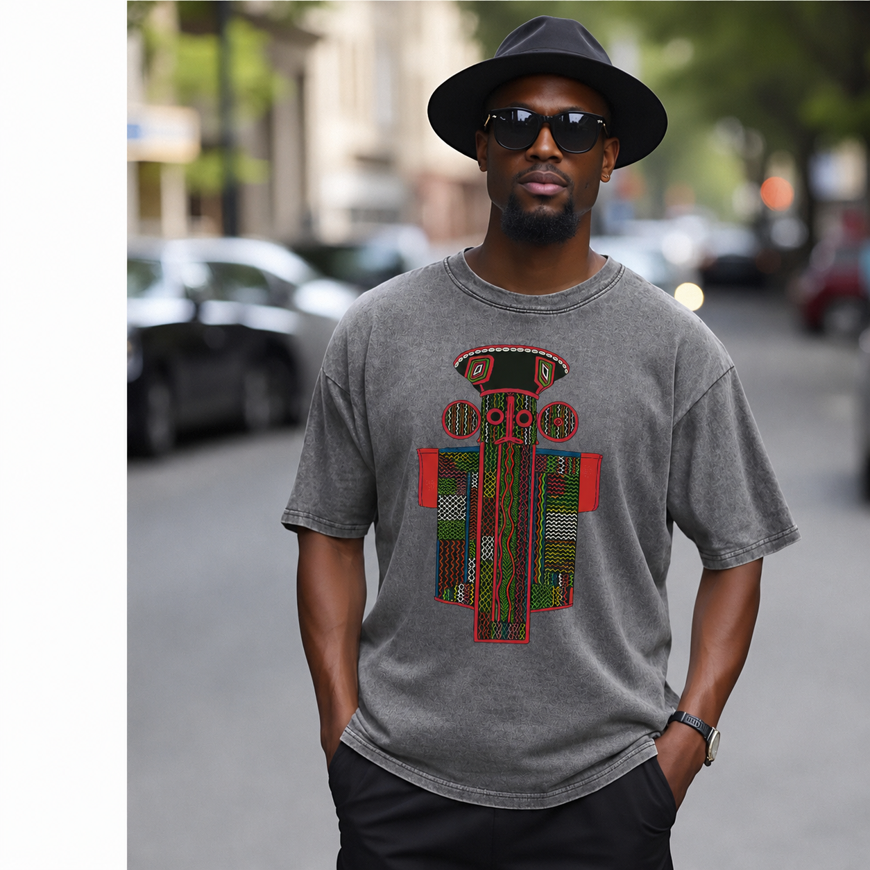 A man wearing a gray t-shirt with a colorful graphic, sunglasses, and a hat is standing on a city street.