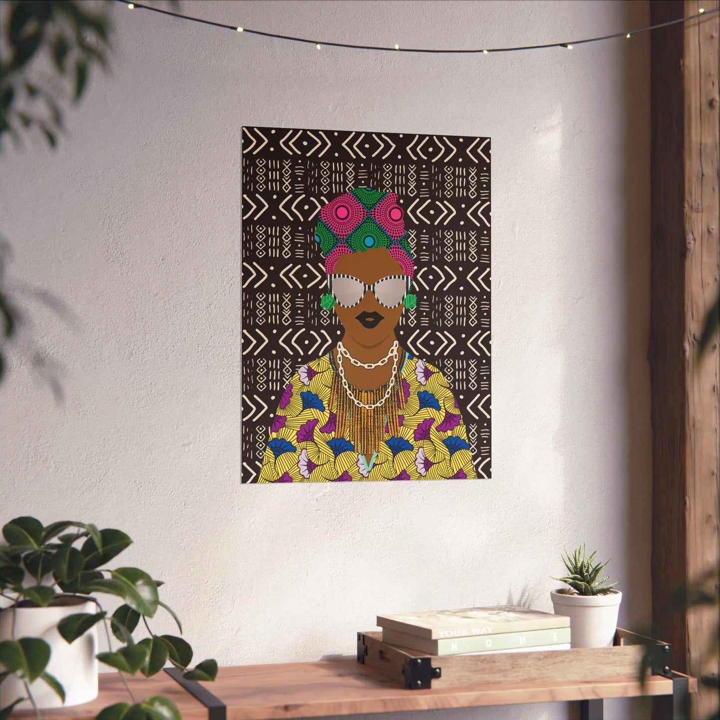 a colorful poster of a woman with a headdress, hanging on a wall above a wooden table with plants and books.