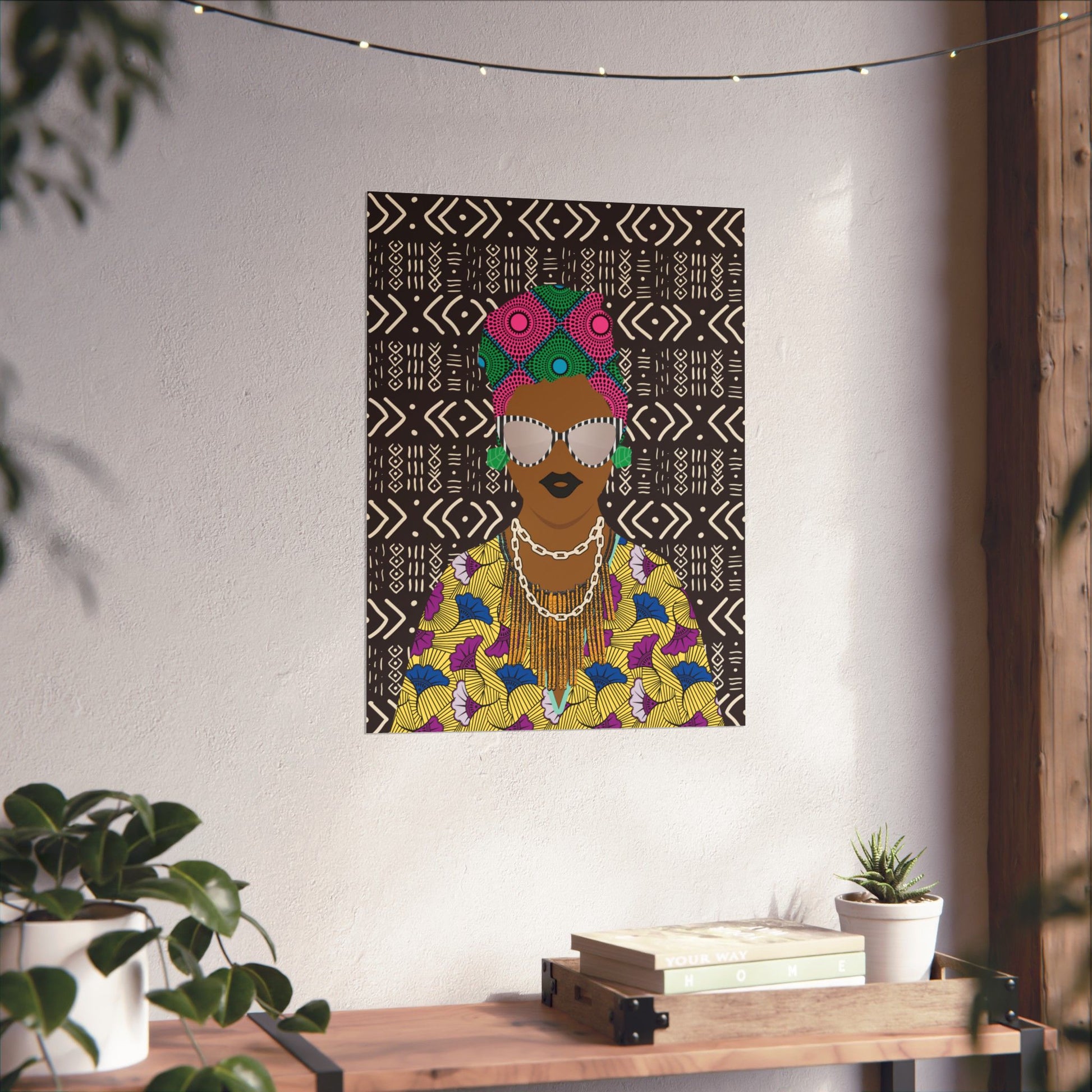 a colorful poster of a woman with a headdress, hanging on a wall above a wooden table with plants and books.