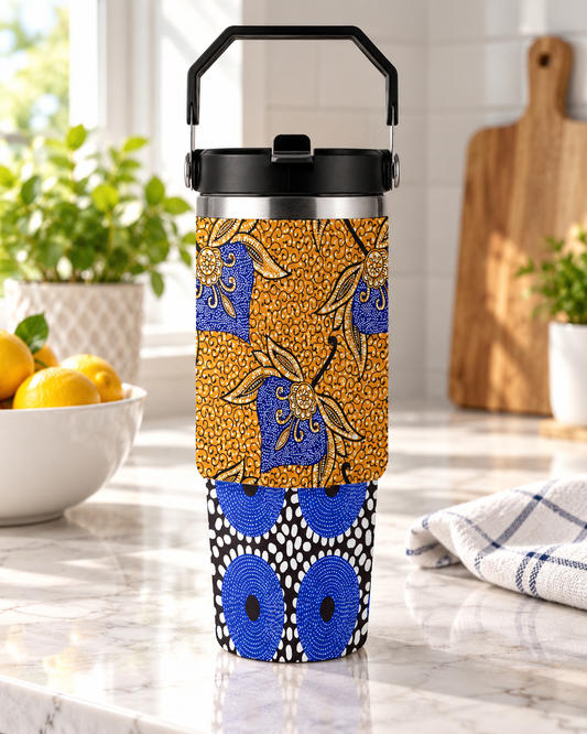 A colorful patterned thermos or thermos cup with a black handle, placed on a kitchen counter with a bowl of lemons and a wooden cutting board in the background.