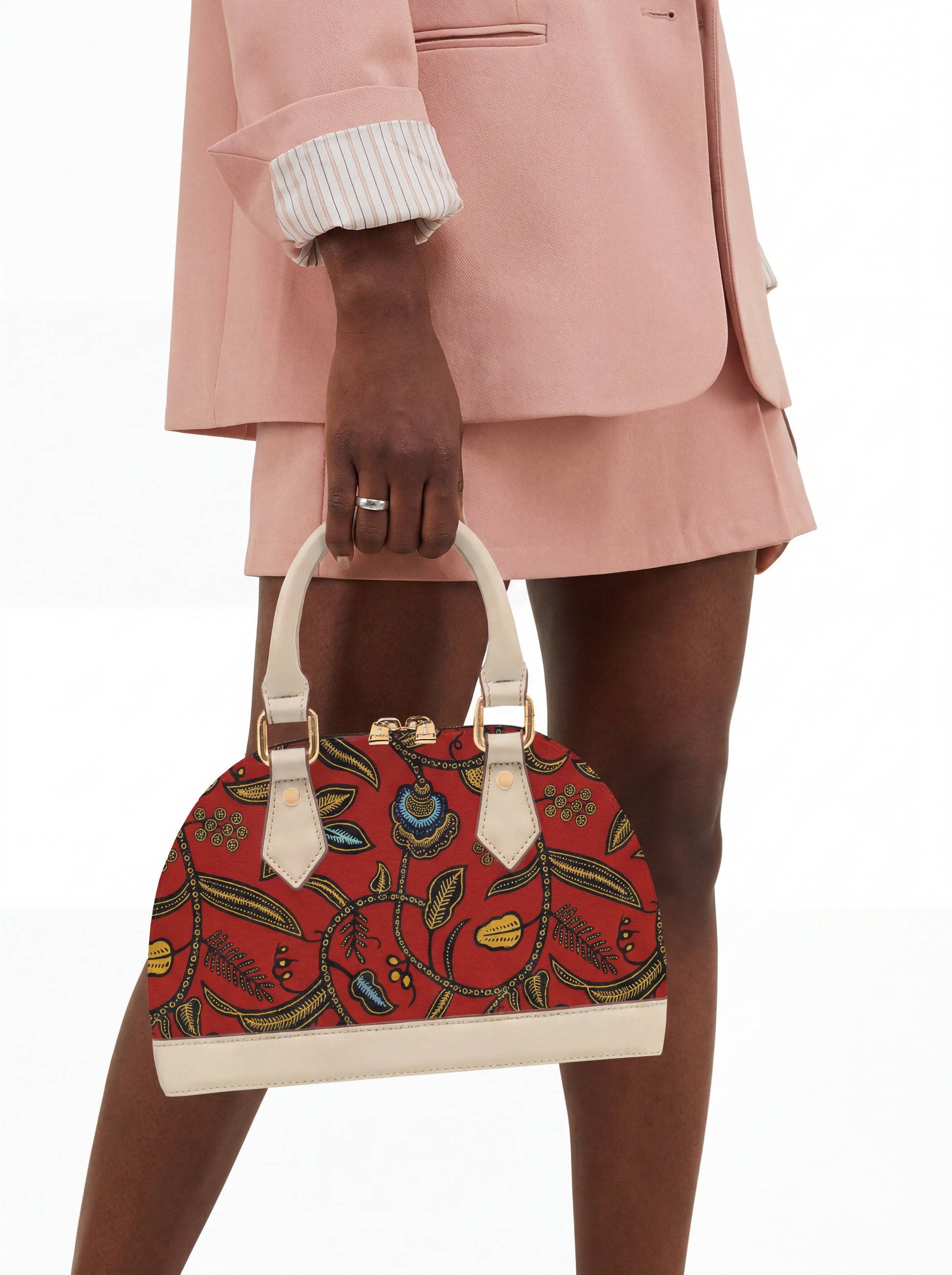A person wearing a pink jacket and skirt is holding a red and white floral handbag.