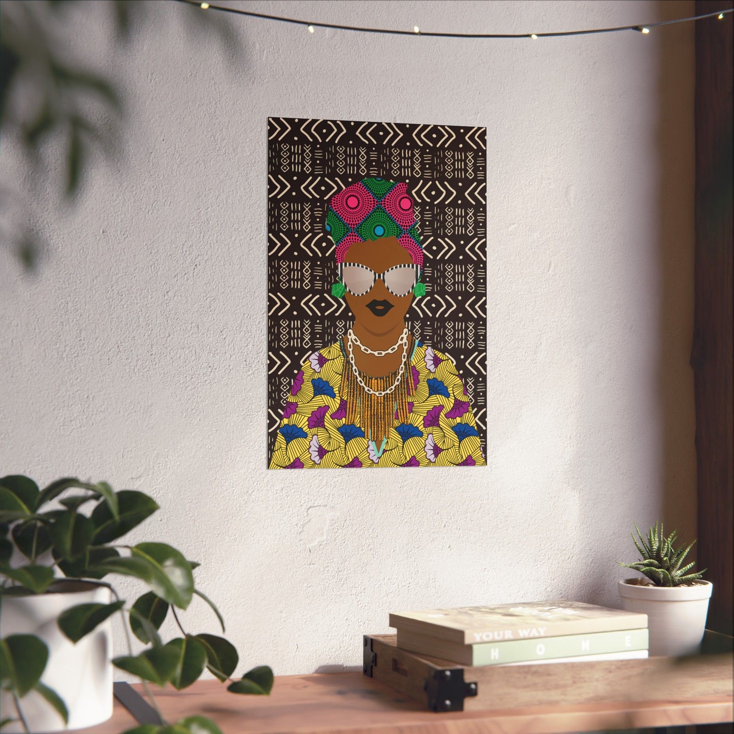 a poster of a woman with a colorful, patterned dress and a headdress, hanging on a wall above a wooden table with plants and books.