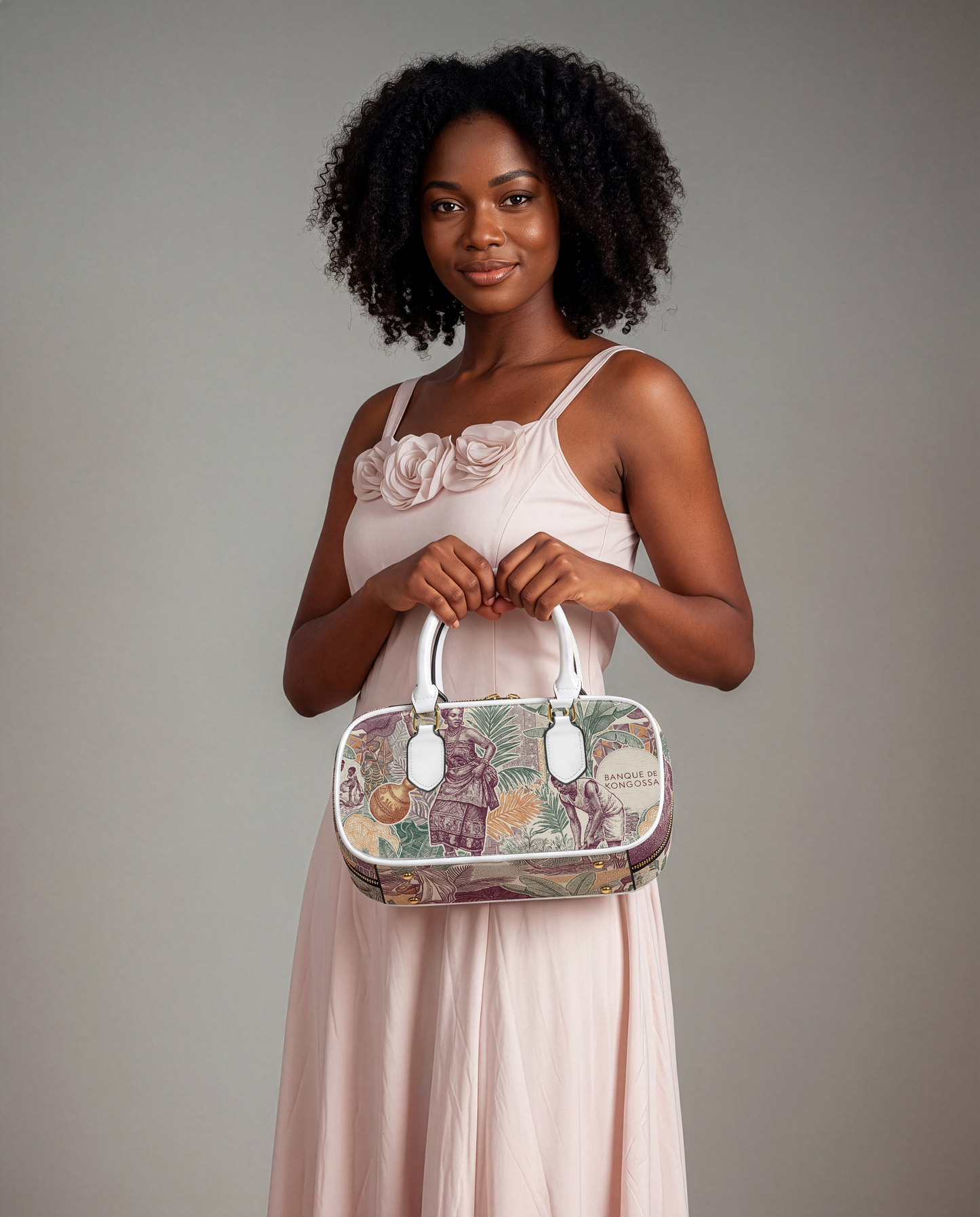 A woman in a pink dress holding a floral handbag stands against a gray background.