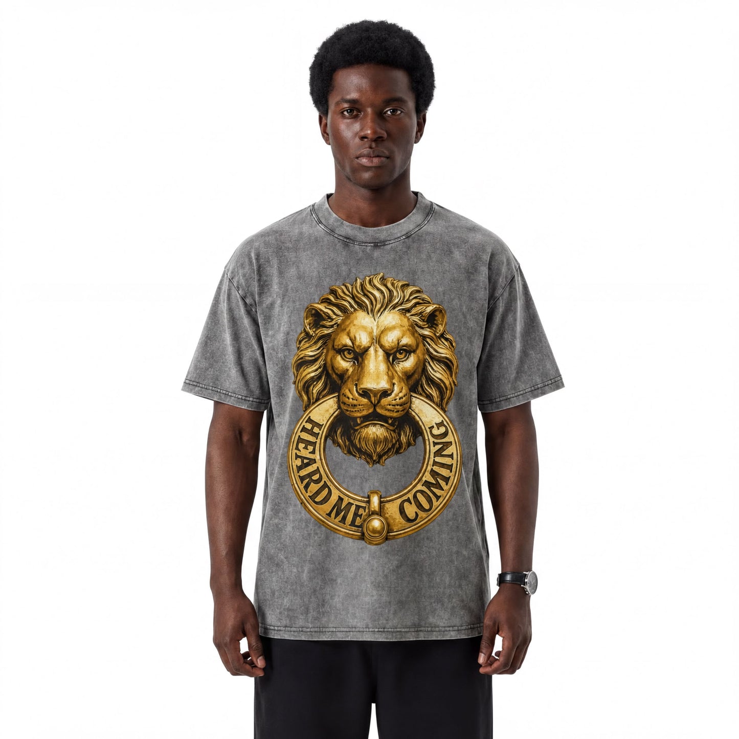 A man wearing a gray t-shirt with a gold lion's head design and the text "HEARD MEC COMING" printed on it.