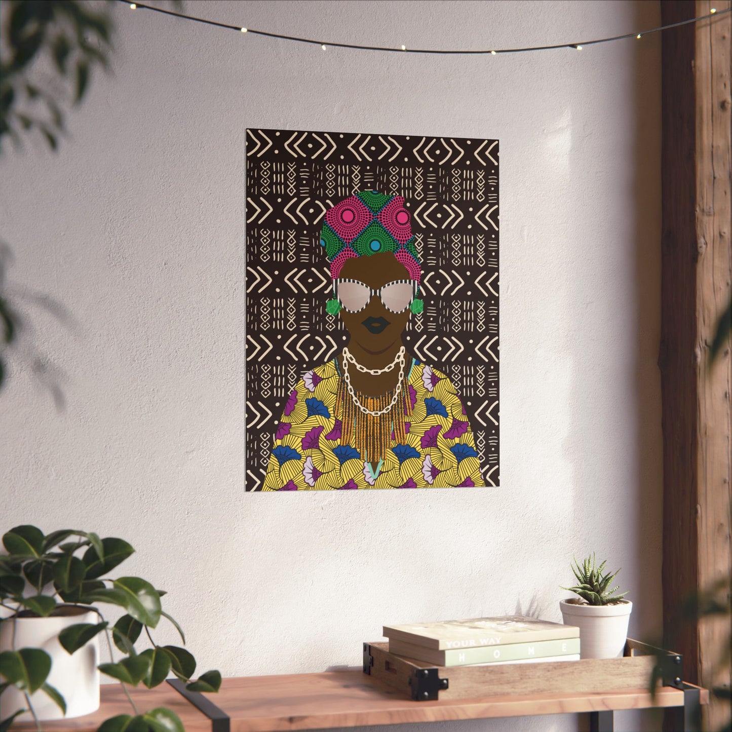 a colorful, abstract portrait of a person with a headdress, hanging on a wall above a wooden table with plants and books.