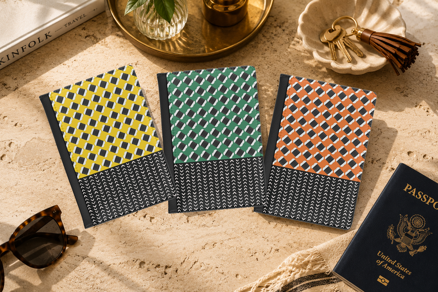 three colorful notebooks with unique geometric patterns, placed on a table alongside a passport, a keychain, and sunglasses.