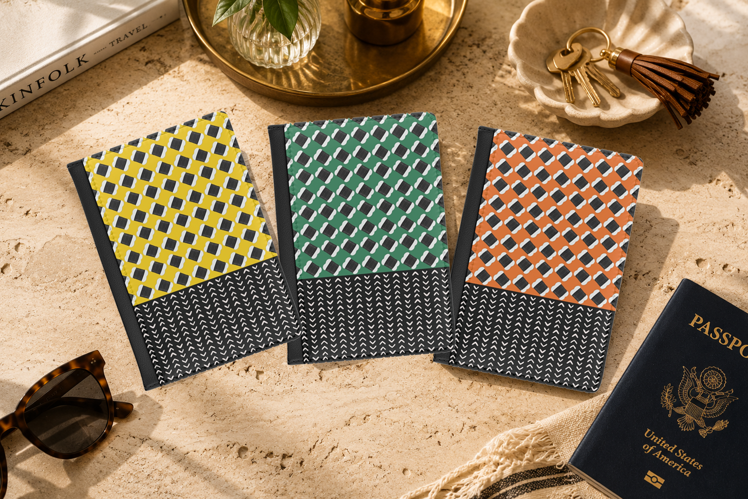 three colorful notebooks with unique geometric patterns, placed on a table alongside a passport, a keychain, and sunglasses.