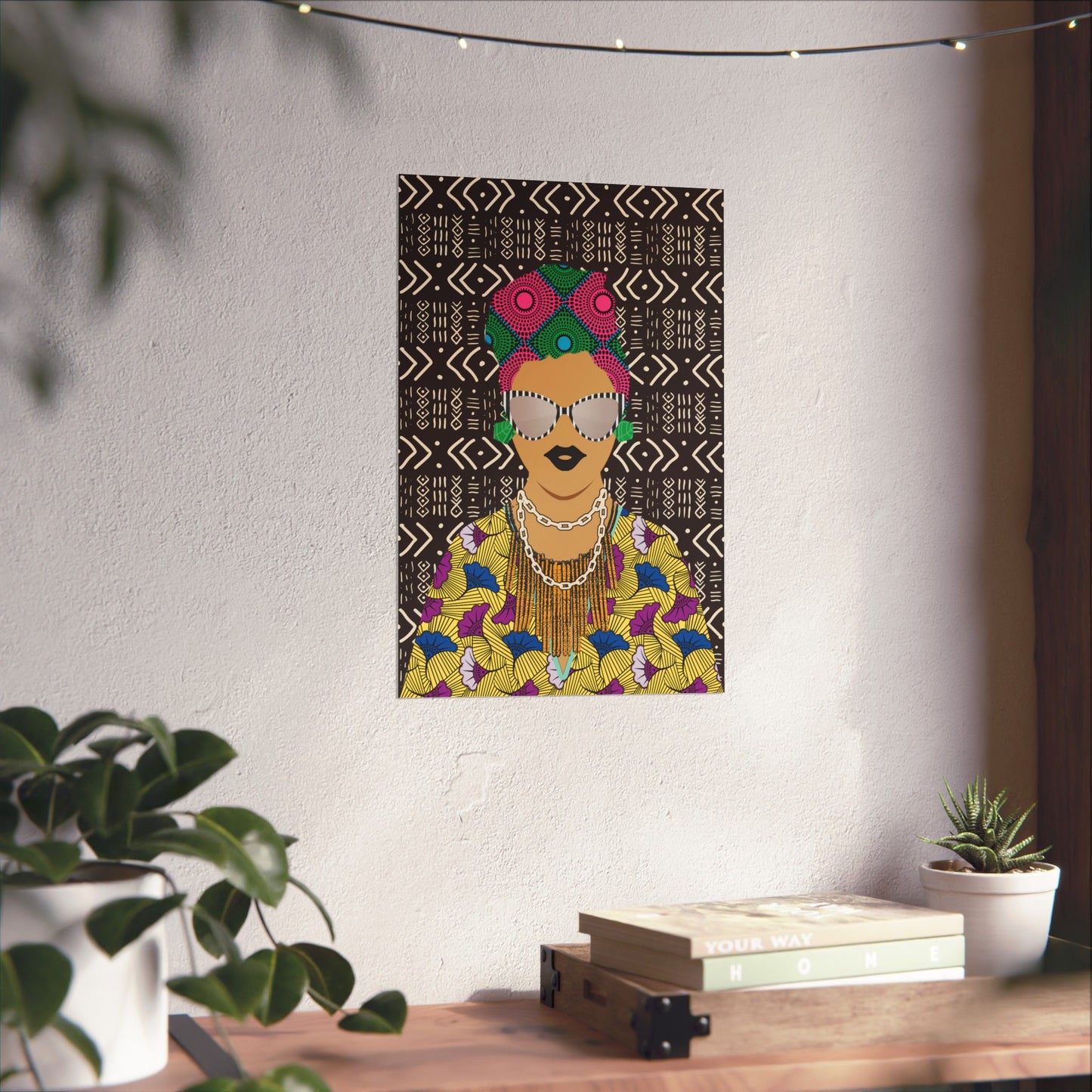 a colorful poster of a woman with a floral pattern and a headdress, hanging on a wall above a wooden table with plants and books.