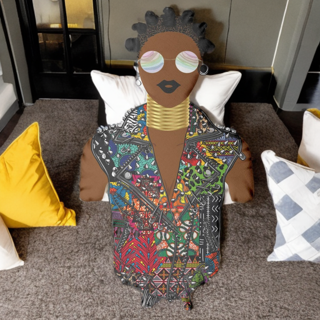 A colorful, patterned doll with a black headpiece and large sunglasses sits on a gray carpet, surrounded by various pillows.