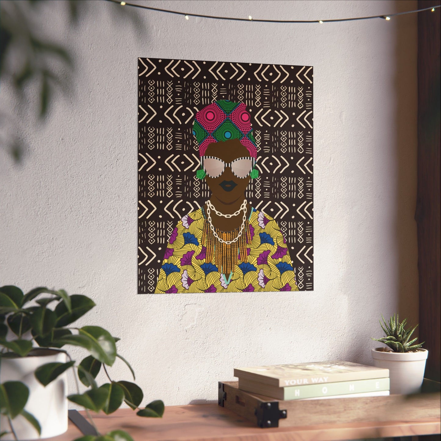 a wall art depicting a woman with a colorful, patterned dress and a headpiece, hanging on a wall above a wooden table with a stack of books and a potted plant.