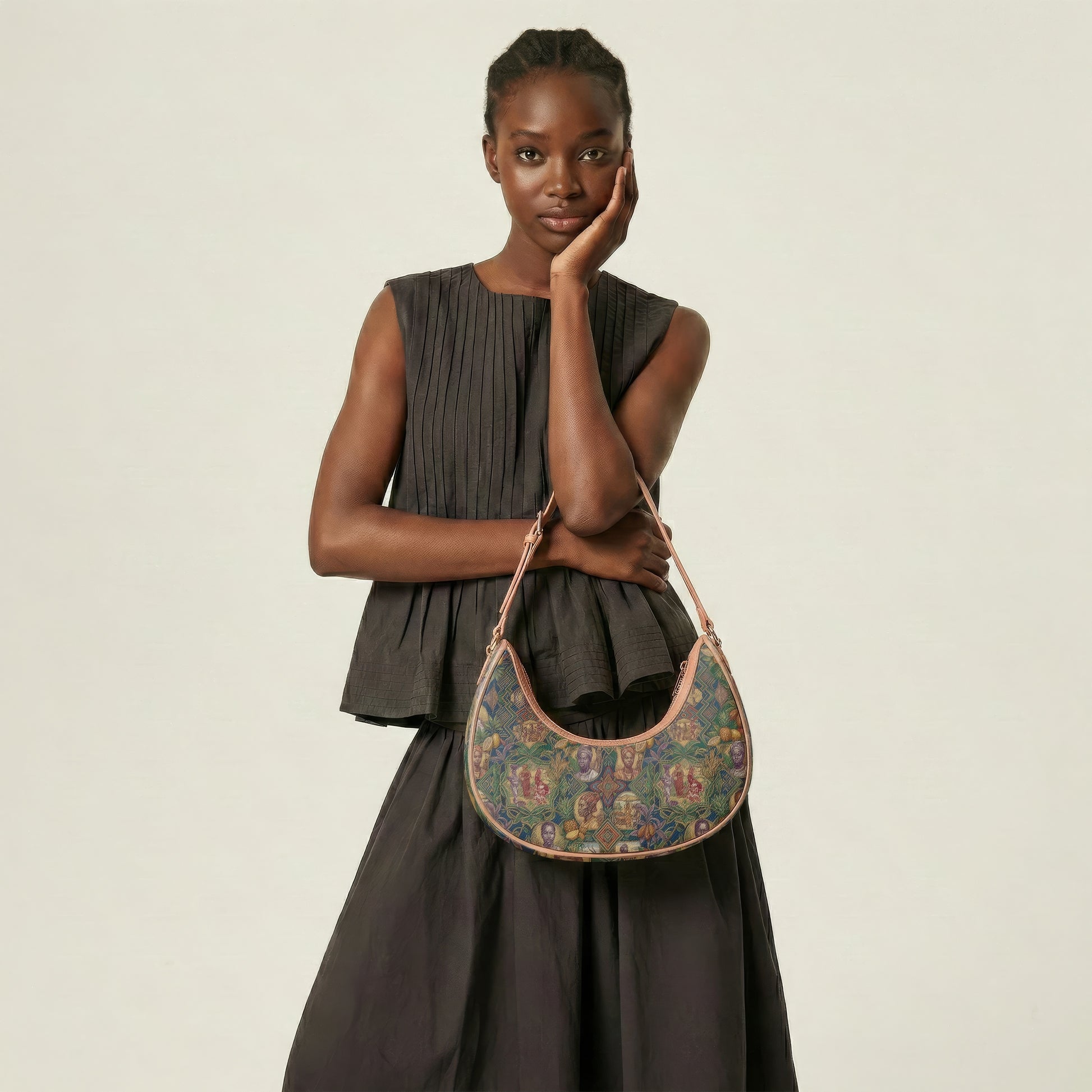 A woman in a black dress stands with her hand on her chin, holding a colorful purse with a floral pattern.