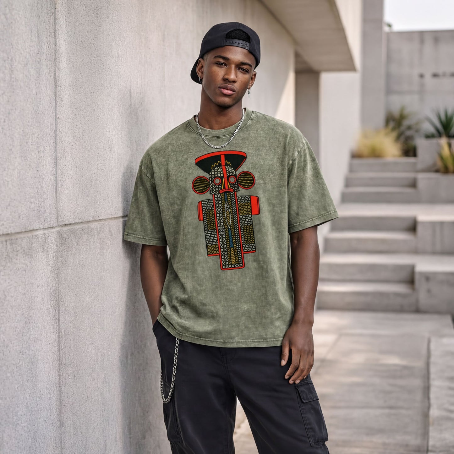 A young man wearing a green t-shirt with a graphic design stands against a concrete wall, leaning against it with his hands in his pockets.