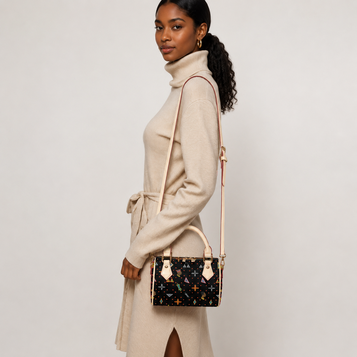 A woman wearing a beige sweater dress and carrying a small black purse with a colorful pattern stands against a plain background.