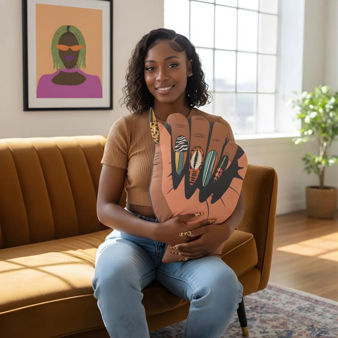 A woman sits on a brown couch, holding a large hand-shaped object with colorful nail art designs.