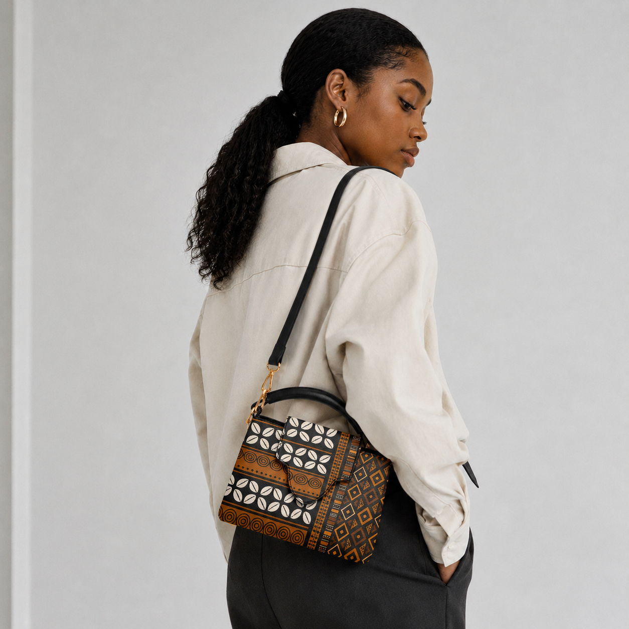 A woman with long dark hair is standing against a white background, wearing a white blouse and carrying a patterned purse.