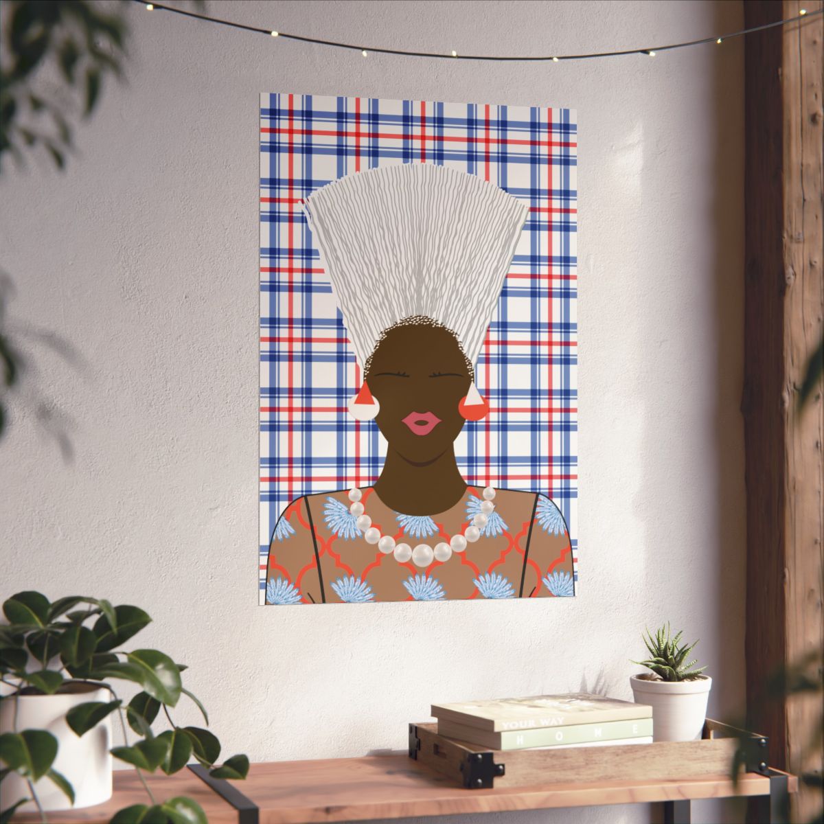 a poster of a woman with a white headdress and a floral patterned dress, hanging on a wall above a wooden table with a plant and some books.