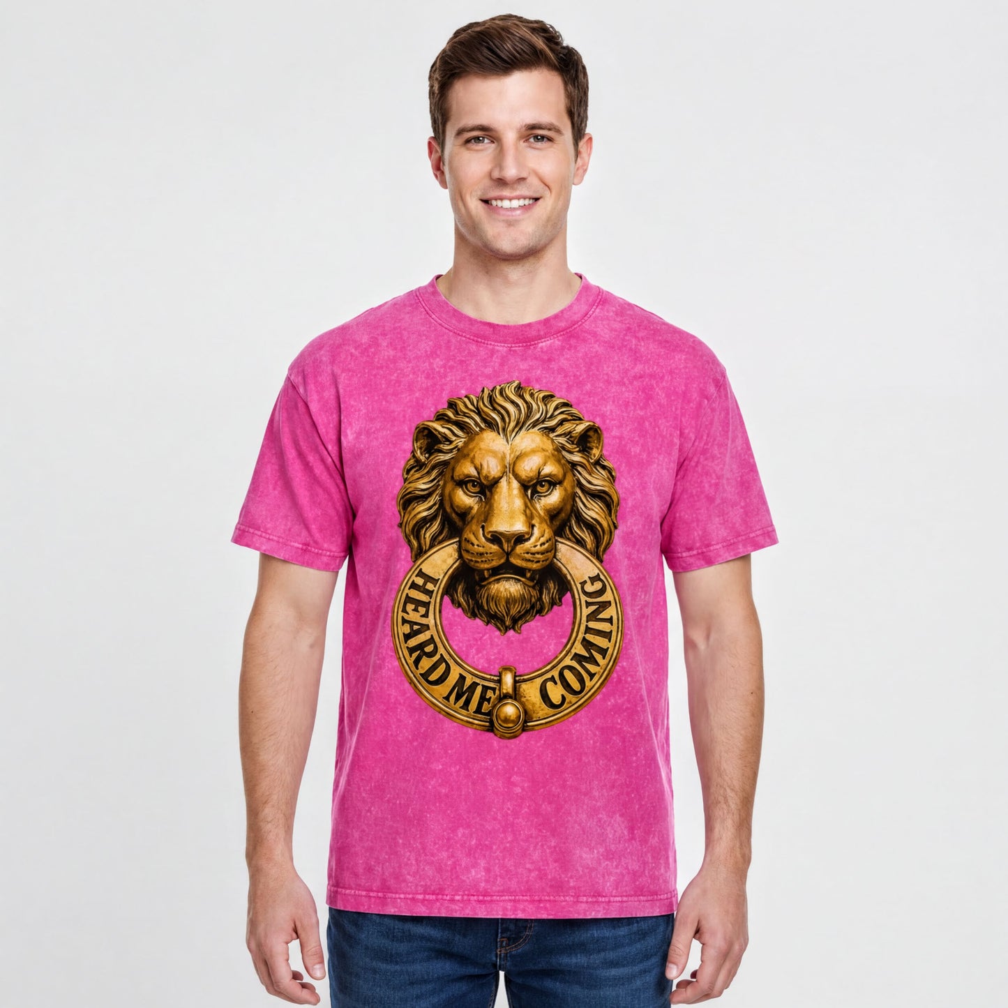 A man wearing a pink t-shirt with a lion's head design and the text "HEARD M' COMING" printed on it.