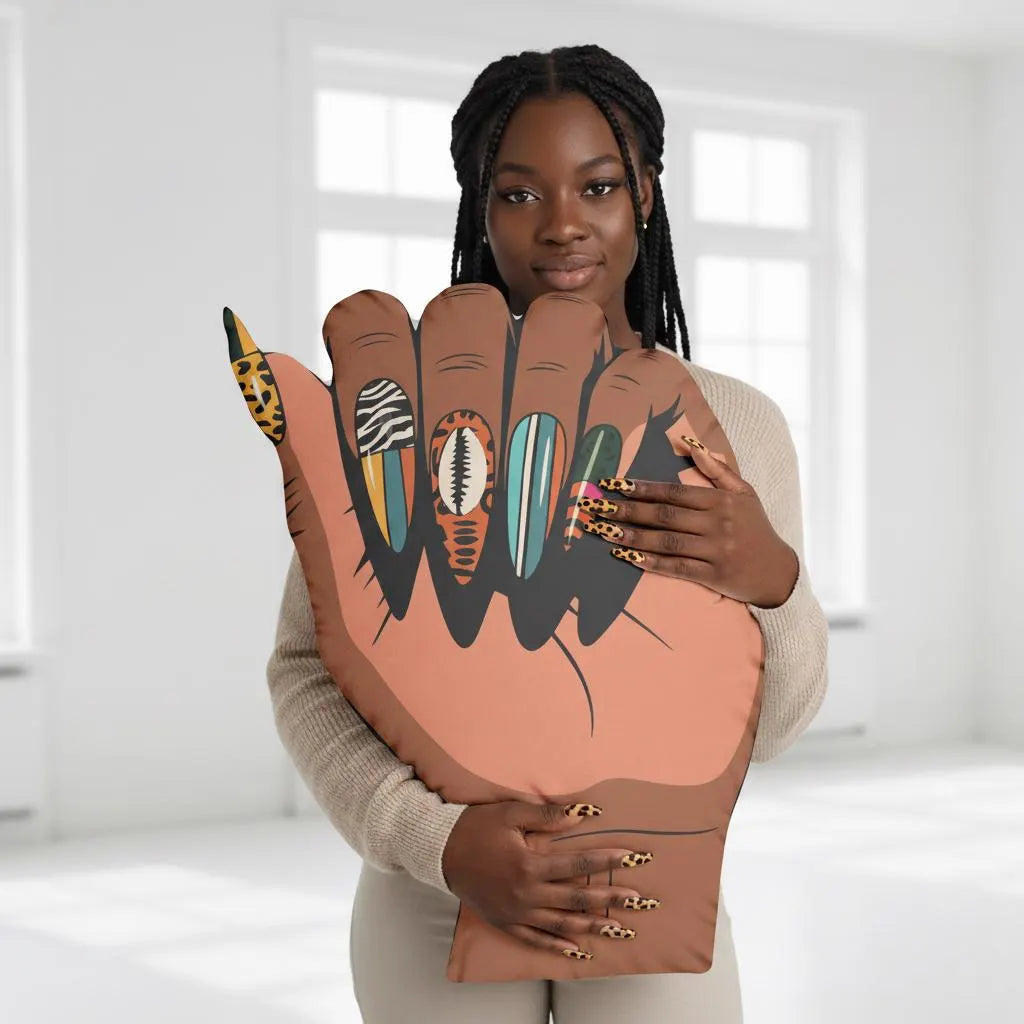A woman with braided hair is holding a large hand-shaped pillow with a picture of a hand with various nail polish designs.