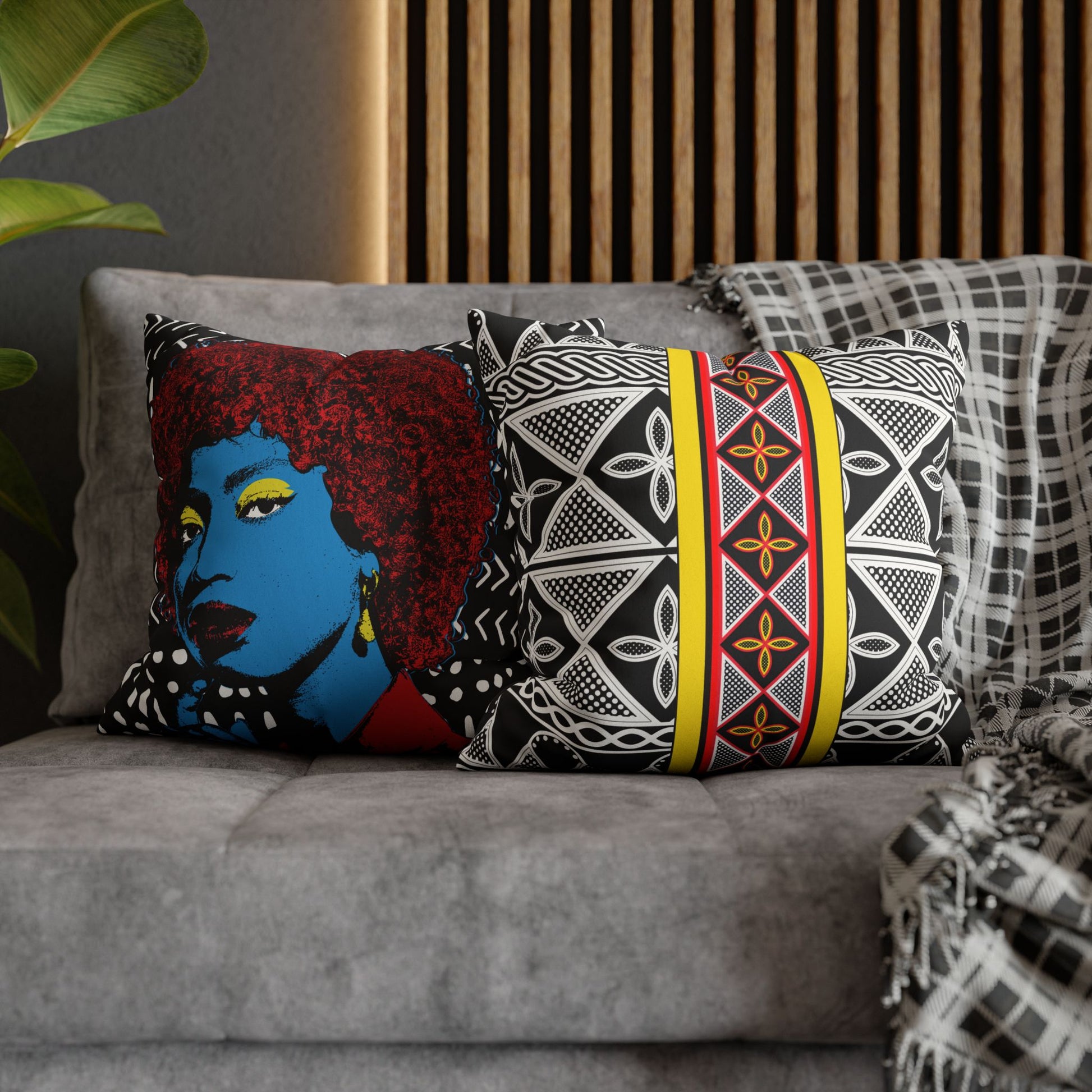 a gray couch with two decorative throw pillows. The pillow on the left has a blue face with red hair, while the pillow on the right has a black and white geometric pattern with a yellow stripe.