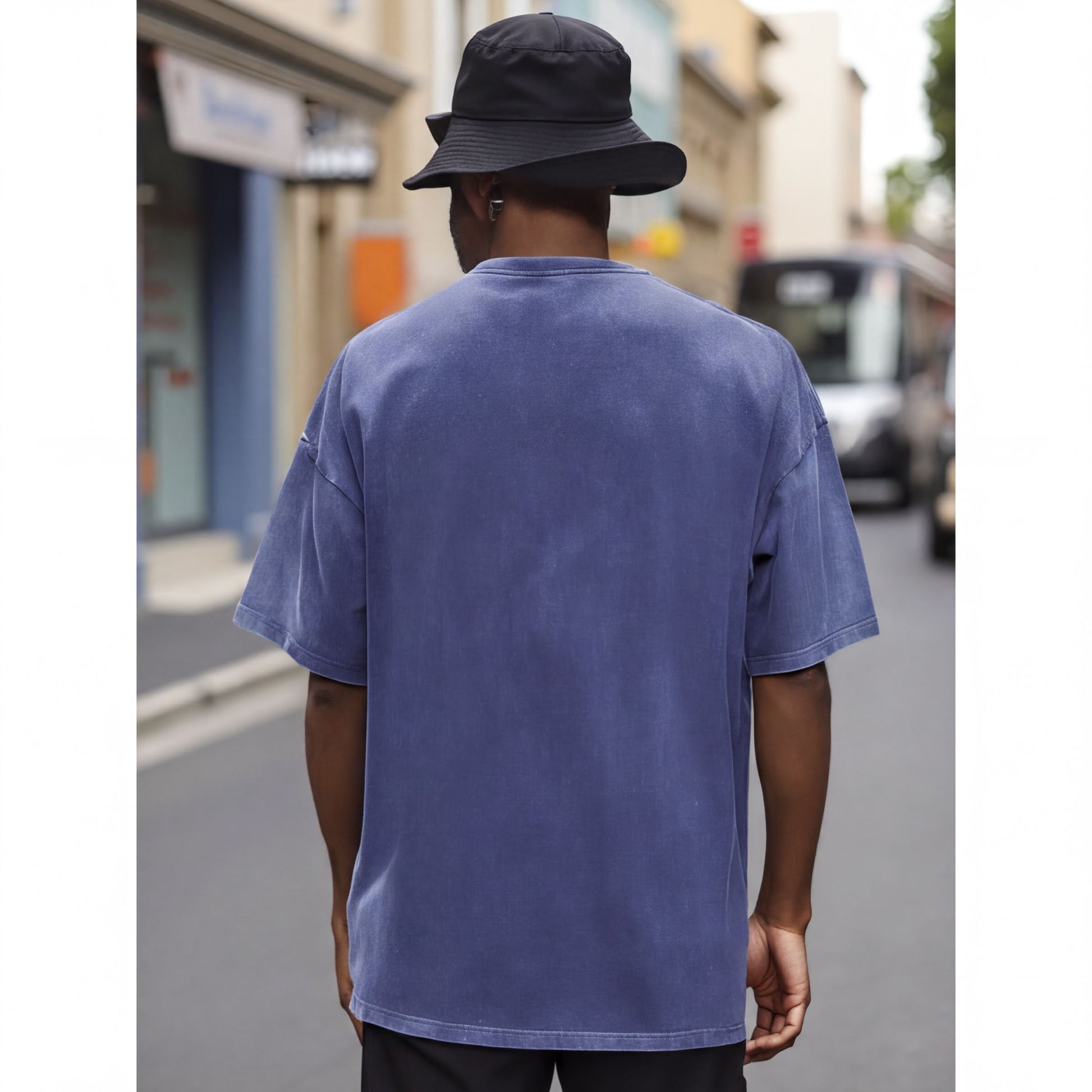A person wearing a blue t-shirt and a black bucket hat is walking down a street.