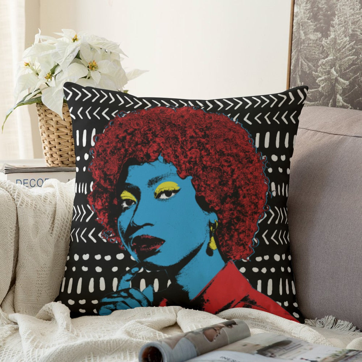 A colorful throw pillow with a portrait of a woman in a red wig, featuring a blue background and white and black geometric patterns.