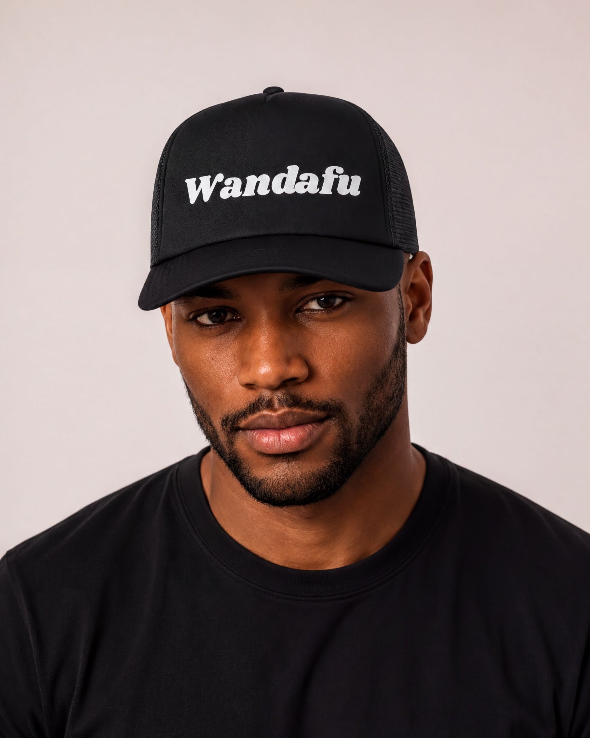 A man wearing a black baseball cap with the word "Wandafu" printed on it.