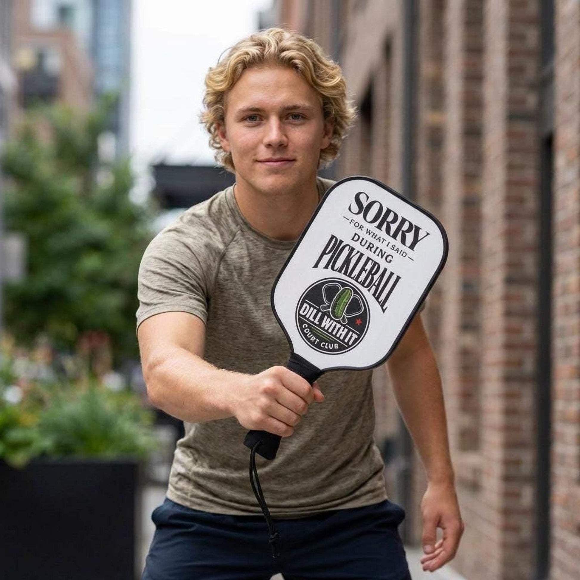 A young man holding a paddleball sign with a humorous message.