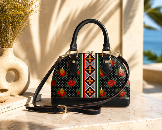 A handbag with a floral pattern and a black leather strap is displayed on a marble surface, with a vase of yellow flowers and a book nearby.