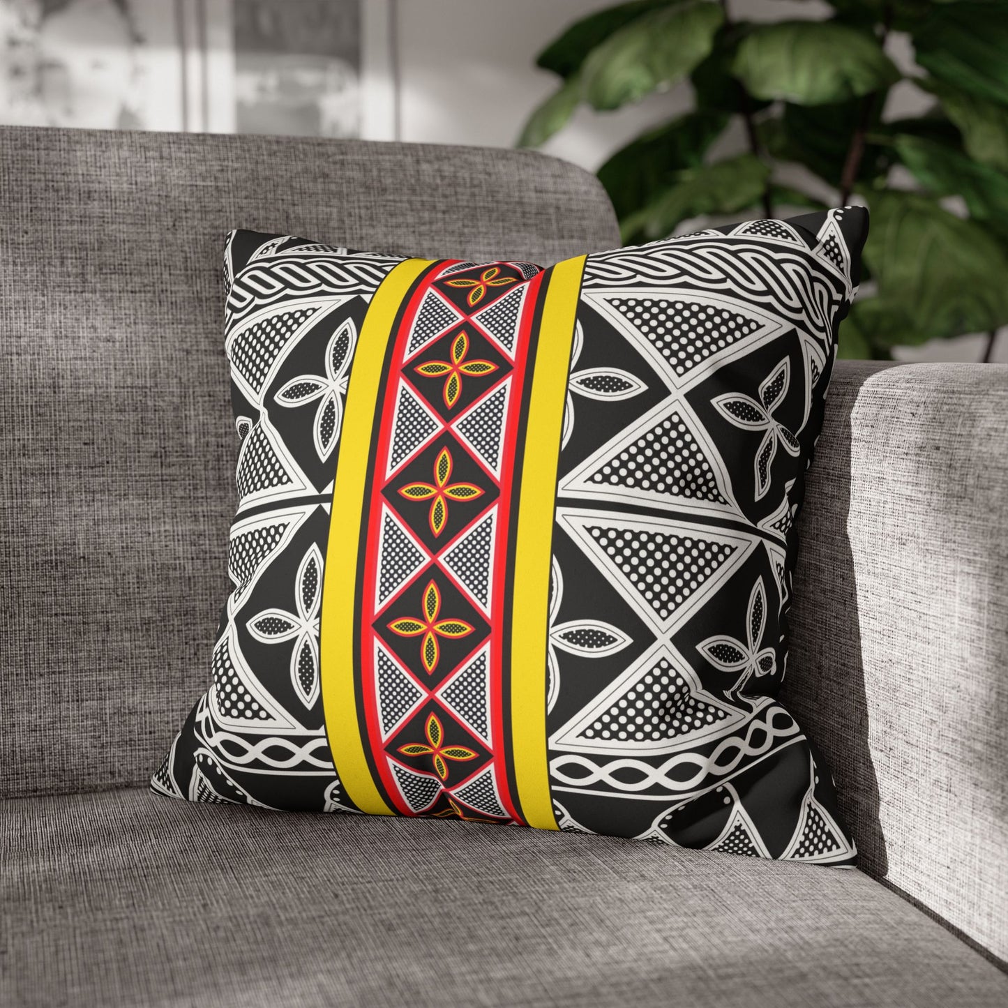 A gray couch with a decorative throw pillow featuring a black and white geometric pattern in red and yellow.