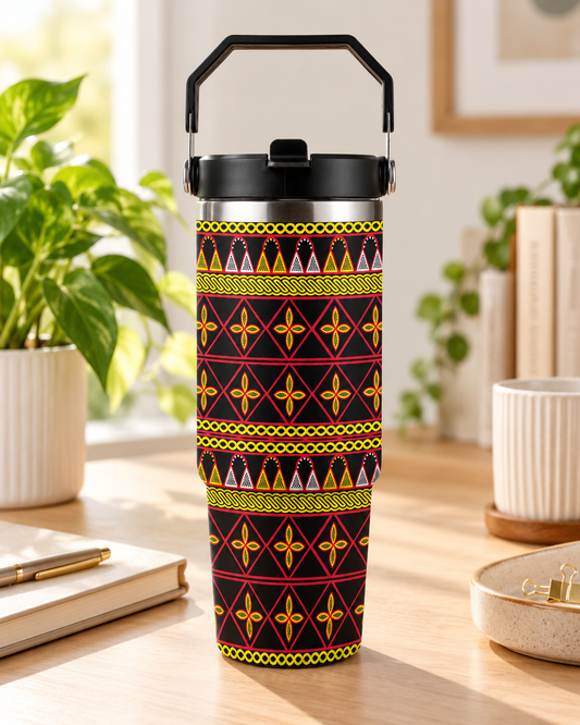 A colorful patterned thermos or thermos cup with a black handle, placed on a wooden surface in a room with potted plants and other decor.