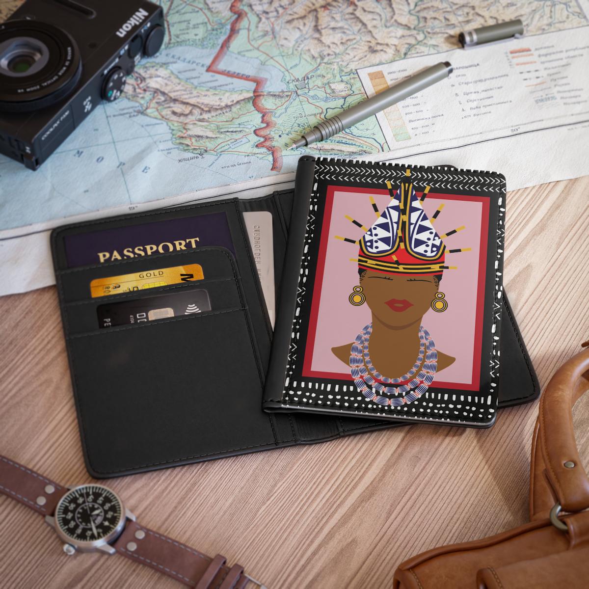a passport holder with a colorful illustration of a woman's face, a camera, a pen, a map, a wallet, a watch, and a purse on a wooden surface.
